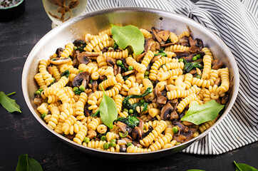 Fusilli pasta with spinach and mushrooms on a pan. Vegetarian / vegan  food. Italian cuisine.