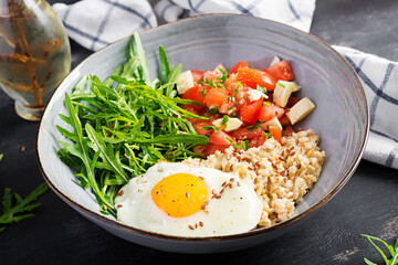 Breakfast oatmeal porridge with fried egg, tomato salad, arugula and flax seeds. Healthy balanced food.