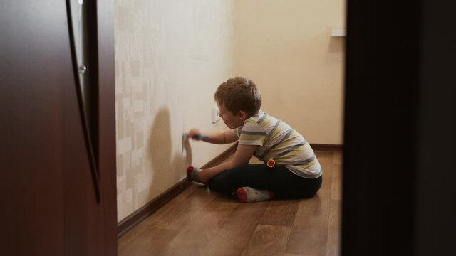 Caucasian child, boy sits near a wall and draws on wallpaper with blue felt-tip pen, marker