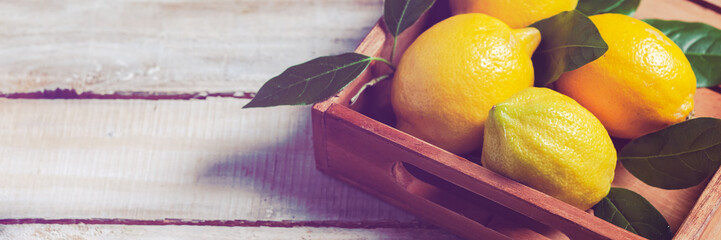 Ripe yellow lemons with leaves in wooden box. Ingredients for refreshing summer beverage - homemade lemonade. Close up, macro view. Wooden rustic background. Copy space for your text. Tonned. Banner