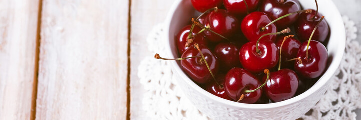 Sweet ripe red cherry in white bowl on vintage napkin. Summer natural low calories dessert. Wooden background. Close up macro. Copy space for text. Banner