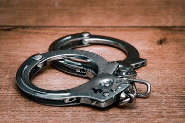 Obraz premium Handcuffs on a wooden background. Close-up. Police handcuffs. The concept of punishment for a crime.