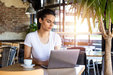 Young female with cute smile sitting with portable net-book in modern coffee shop interior during recreation time, charming happy woman student using laptop computer to prepare for the course work