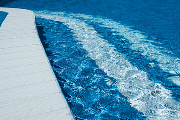 Steps to the pool, blue clear water in the outdoor swimming pool, safe descent to the pool, close-up steps through the water