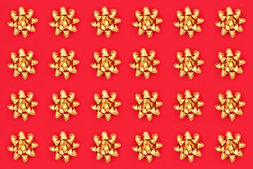 Christmas gold ribbon bows composition on red background. Repeating pattern for the festive season, top view, flat lay.