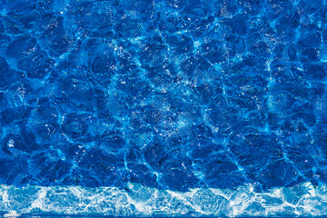 Swimming pool, blue clear water in the outdoor pool, with sun flare on the surface. Background of blue water in the pool
