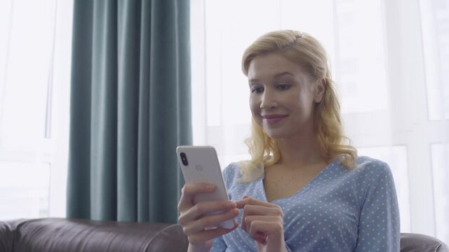 Happy attractive woman reading message on smartphone, watching photos online