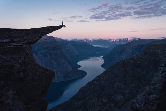 A woman sitting on the edge of Trolltunga in a beautiful morning sunrise in summer season, Odda town, Norway, Scandinavia