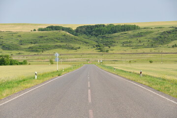 paved road through green fields and hills in summer