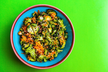 Fresh vegetable salad on a green background. Salad of fresh cucumbers, lettuce, carrots, green onions and sesame seeds. Diet salad
