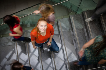 Obraz na płótnie Canvas At the university/college - Students rushing up and down a busy stairway - confident pretty young female student looking upwards