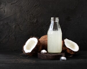 Coconut water with ice in a glass bottle and coconut halves on a black background with space for text.