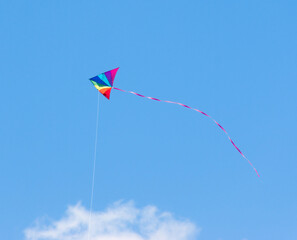 Fototapeta na wymiar Child's toy kite in rainbow colors flying in a clear blue summer sky
