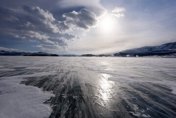 Beautiful clouds over the ice surface and windy snowdrift on a frosty day. Frozen Lake Baikal.