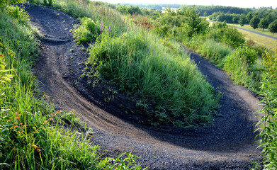 single trail path on mountain sprung bikes sharp bends bends jumps in forest or meadow. dark gravel...