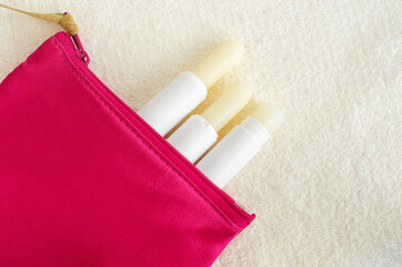 Three lipbalms in the small make-up pouch. Natural lip care concept. Top view, flat lay, copy space.