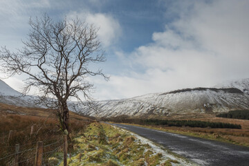 Road in a mountains, The Gleniff Horseshoe loop drive in county Sligo, Ireland, Mountains covered with snow, Winter season. Cloudy sky.