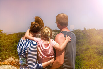 A happy family of mom, dad and little daughter are standing on the top of the mountain and watching the local landscape.