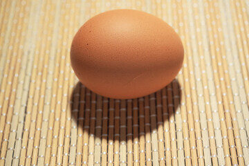 One brown egg on a simple bamboo table cloth. Poultry product.