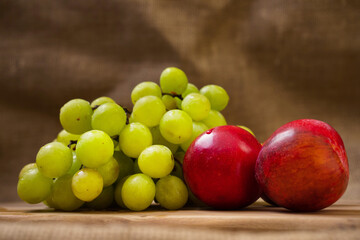Fresh juicy white grapes and nectarines on a wooden board, Hessian backdrop, Still life. Selective focus.