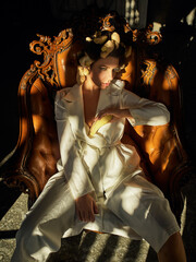 a beautiful girl in a white pantsuit with ginger is sitting in a brown leather chair - 357162810