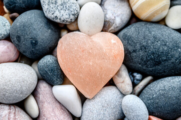 Fototapeta na wymiar Pink stone heart with rock stones in background. Symbol of love.
