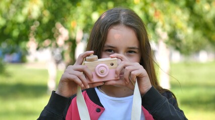 Girl 11 years old takes pictures with a toy wooden pink camera.