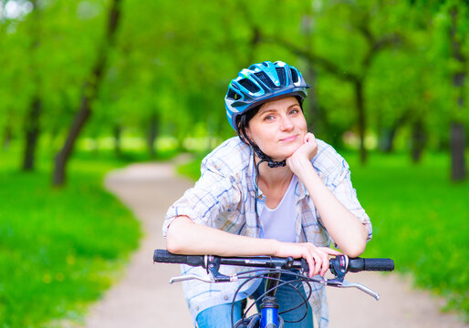 Girl in a bicycle helmet oclocotilas on a bicycle handlebar and looks at the camera on a path in a summer park
