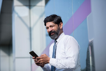 Naklejka na ściany i meble A portrait of businessman with smartphone standing outside the office