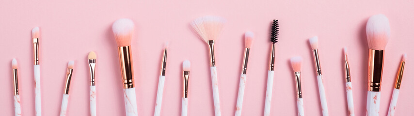 Set of makeup brushes in row on pink background. Professional cosmetics tools collection. Wide...
