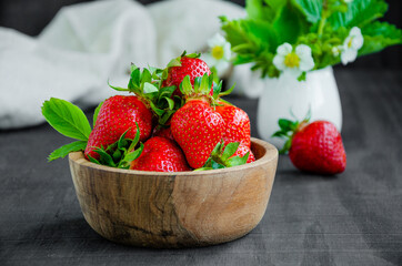 Fresh strawberries in a wooden bowl on a dark wooden background. Horizontal, copy space.