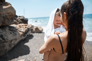Fototapeta na wymiar a mother embraces a smiling child on the beach against the background of the sea