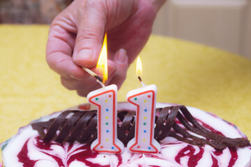 Candles on cake in form of number 11 and hand lighting them with a match