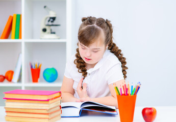 A girl with down syndrome enthusiastically reads a book that lies in front of her on the table. Affordable education for everyone concept