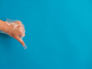 Hand with plastic glove with thumb down on blue background with c