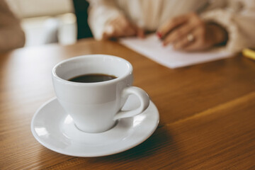 Close up coffee cup in front of female hands writing notes during creative meeting, discussion, project working in office. Concept of finance, business, girl power, inclusion, diversity, feminism.
