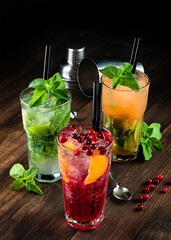 three alcoholic cocktails mojito and cranberry or lingonberry cocktail on a wooden background