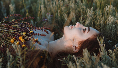close-up face of beautiful girl lying on the grass with bouquet of wildflowers, young woman with...