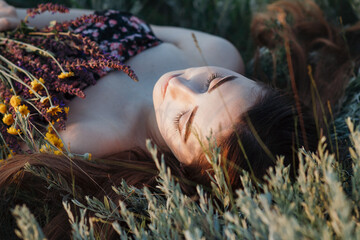 close-up face of beautiful girl lying on the grass with bouquet of wildflowers, young woman with long hair on nature,summer tender photo in village