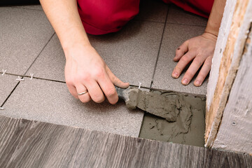 A man puts cement with a spatula for laying tiles. Finishing is one of the stages of repairing an apartment. Hands in the process.