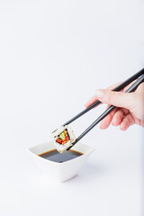 Female dipping tasty sushi makaki or uramaki with chopsticks into bowl with soy sauce on white background. Space for copy.