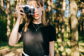 Portrait of beautiful young female photographer with short fair hair in black t-shirt stands with her camera