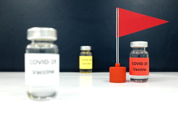 Selective focus of covid-19 vaccine vial beside a red flag. Coronavirus vaccine candidate development race and competition winner concept.