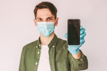 Fototapeta na wymiar Portrait young man in protective glove and medical face mask hold smart phone with empty copy space isolated on white background. Happy man with cell phone in hand. Digital mobile contact less payment