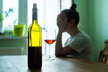 woman drinks red wine and cries. foreground glass bottle with cork. blurry. concept female alcoholism, treason, grief. depression, stress. blurry