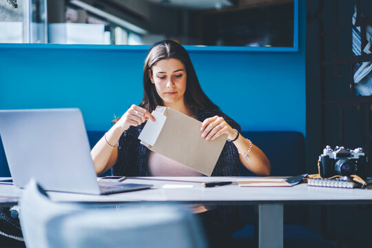 .Cheerful young woman with brunette hair holding envelope in hands in coworking space