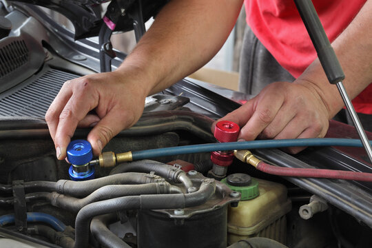 Mechanic charging air condition unit at modern car, closeup of workers hands and equipment conected to car engine, red and blue clucth couplings