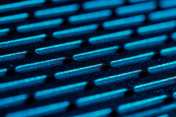Regular pattern of elongated holes in a rough plastic surface. Illuminated blue, harsh side light. Macro shot of textures, abstract and dark.