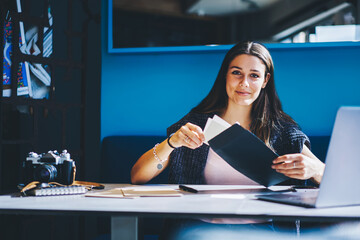 .Cheerful young woman with brunette hair holding envelope in hands in coworking space