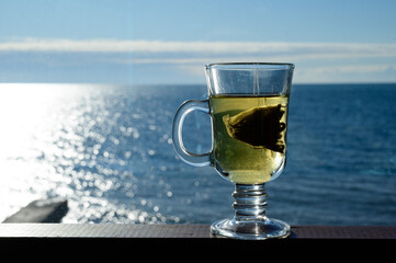 Transparent glass mug with a bag of green leaf tea on a background of the sea.